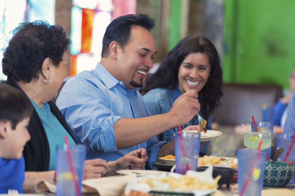 A man sitting with friends at a table, putting food on a plate.