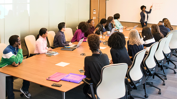 People sit around a conference table and watch a person draw on a whiteboard