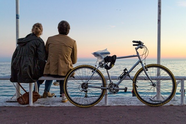 a female and a male being mindful on a bench next to a bike watching the sunset.